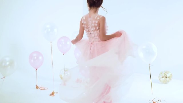 wonderful fascinating lady whirls and dances in a light pink flying and flailing dress, children's joy in an adult girl, a lot of helium balloons on the floor and in the air in front of white studio