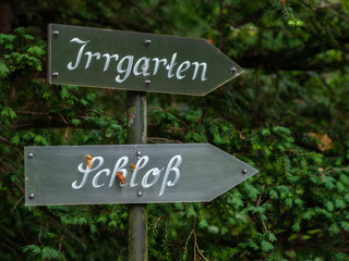 Signpost in front of green vegetation - german signs read 'Maze' (top) and 'Castle' (bottom)