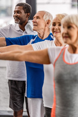 Fototapeta premium smiling senior multiethnic sportspeople synchronous exercising at sports hall