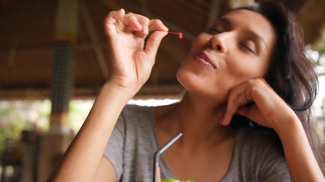 Attractive Young Mixed Race Tourist Girl Eating Pickled Chery from Tropical Cocktail at the Restaurant. 4K, Slowmotion. Bali, Indonesia.
