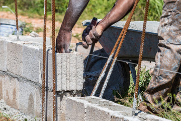 Hands of a black adult male mason/bricklayer laying cement block and using trowel to remove excess...