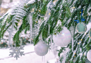 The snow-covered Christmas tree is decorated with white balls, icicles and a garland.