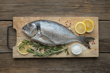 Fresh dorado fish with lemon slices, salt and rosemary on wooden cutting board. Top view.