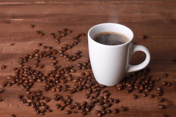 Steaming hot coffee and beans on vintage wooden table. Coffee break concept. White cup, winter drink, espresso, side view