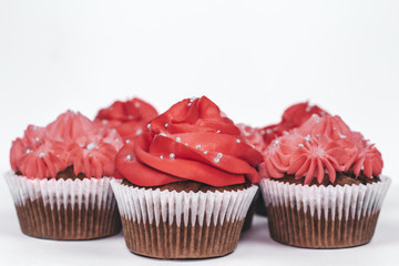 Several delicious chocolate cupcakes with red and pink creamy icing on isolated white background.