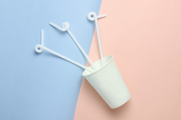Paper coffee cup with cocktail straws on a colored pastel background, top view, minimalism..