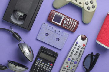 Retro objects on violet background. 3d glasses, audio cassette, video cassette, gamepad,calculator, tv remote, headphones, push-button phone. Flat lay..