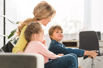mother with adorable kids sitting on sofa and using remote controller