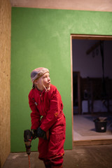 Kind mit rotem Anzug rührt in Farbe vor grüner Wand