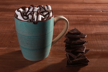Cocoa, marshmallow and stack of chocolate pieces on vintage wooden table. Coffee shop or hot chocolate concept. Blue cup, winter drink, side view, confection