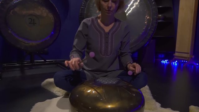 Woman is playing meditative instrument tank drum in a dark meditation room.