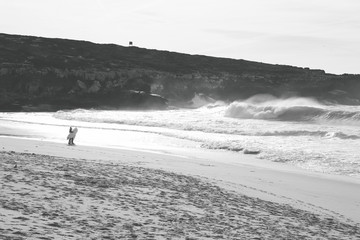 Two surfers in a beach at the sunset with a wave in background