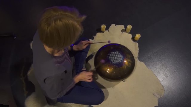 Woman is playing meditative instrument tank drum in a dark meditation room.