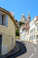 A narrow sloping street bordered with old townhouses in Marseille, France, going up to Notre-Dame de la Garde basilica on top of the hill.
