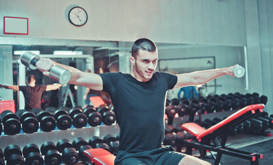 Fototapeta na wymiar Athletic young man exercising his shoulders and doing side raises with pair of dumbbells at gym