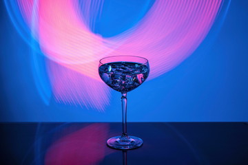 Beautiful view of alcohol drink with ice cubes in crystal glass on colorful background. 