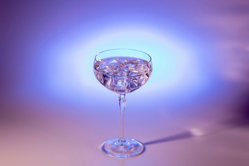 Beautiful view of alcohol drink with ice cubes in crystal glass on colorful background. 