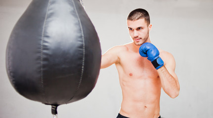 Handsome concentrated male boxer trains hand punches with a punching bag..