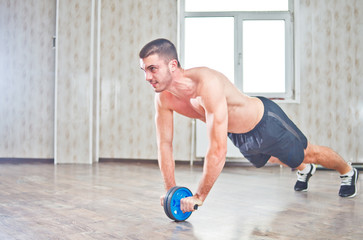 Handsome sportsman workout with abdominal ab roller at hall with window