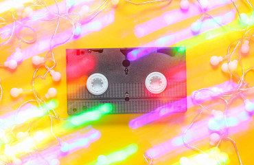 Retro vhs video tape with bright glowing led garlands on a yellow background. 80s, Light effect. Top view, minimalism. .