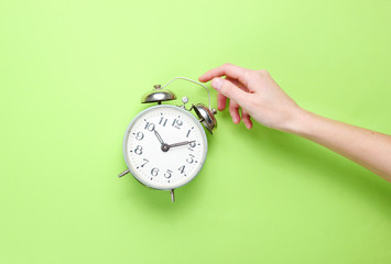 Female hand takes alarm clock on green background. Top view. Time to wake up. Minimalism.