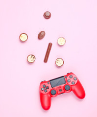 Red gamepad and chocolate candy on pink pastel background