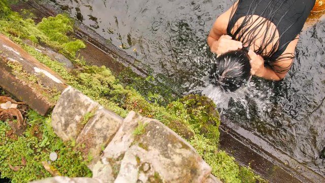 Young Woman Praying at Holy Spring Water Temple. Traditional Balinese Hindu Spiritual Ceremony of Purification. 4K Slowmotion. Gugung Kawi, Bali, Indonesia.