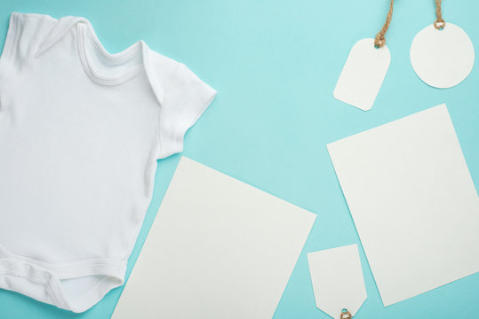 Layout Flat Lay a white baby bodysuit on a blue background with white postcards and tags. Choose design and placement of logos, advertising