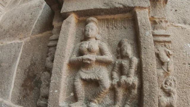 Female giant with naked breast and man with drum carved in stone on the wall of ancient temple