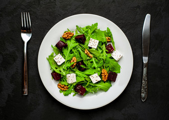 Salad of arugula, cheese, beet, walnut, on the background of slate, stone or concrete.