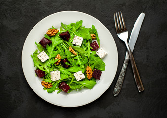 Salad of arugula, cheese, beet, walnut, on the background of slate, stone or concrete.