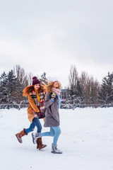 Two curly Caucasian stylish girls sisters are walking and running through the snow. Rejoice in winter and snow