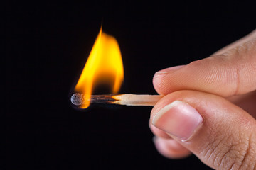 burning match stick in the hand on a black isolated background