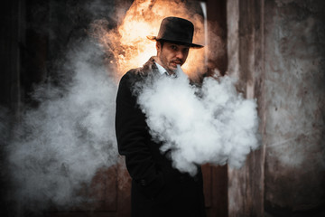 Vaping man in black hat holding a mod. A cloud of vapor.