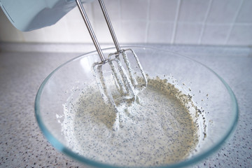 Electric hand mixer with whipped poppy cream.  Mixing white cream in bowl with blender, baking cake. Kneading dough for making cheesecake. Whipped cream on the whisk or beater