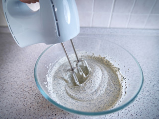 Electric hand mixer with whipped poppy cream.  Mixing white cream in bowl with blender, baking cake. Kneading dough for making cheesecake. Whipped cream on the whisk or beater