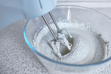 Electric hand mixer with whipped poppy cream.  Mixing cream in bowl with blender, baking cake. Kneading dough, making cheesecake. Whipped cream on the whisk or beater. Glass bowl with mixer and cream