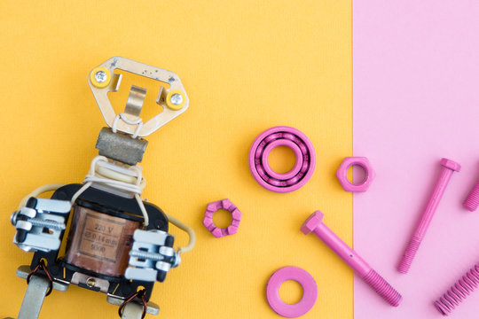 Metal robot, screws and washers, spring, colored with multicolored paint. Colorful background. Pink and yellow. Concept, background, flat lay.  Free space for text.