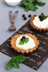 Mini tarts (tartlets) with whipped cream or custard and fresh berries served with mint. Homemade dessert. Grey background. Copy space.