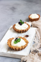 Mini tarts (tartlets) with whipped cream or custard and fresh berries served with mint. Homemade dessert. Grey background. Copy space.