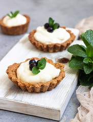 Mini tarts (tartlets) with whipped cream or custard and fresh berries served with mint. Homemade dessert. Grey background. Copy space.
