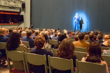 Man appears on stage in theater with many people