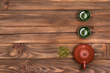Brown ceramic teapot, two dark green special cups and green tea on a dark wooden planked background. Tea ceremony. 
