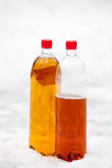 two plastic beer one litre bottles full and half with red caps on white snow background.