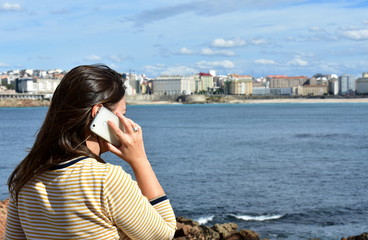Fototapeta na wymiar Woman talking on a smartphone in a bay. Beach, promenade and city view.