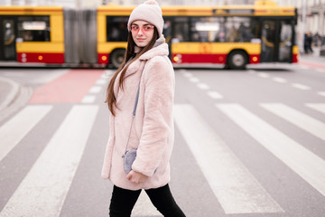 Fashion woman walking on the city street, wear pantone color jaket with pink glasses and look to camera. Copy space. - Image