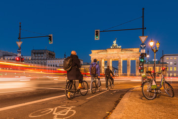 Backside of the Brandenburg Gate at night. Cyclists are waiting at the traffic light. passing cars in long-term exposure. An e-bike is on the roadside