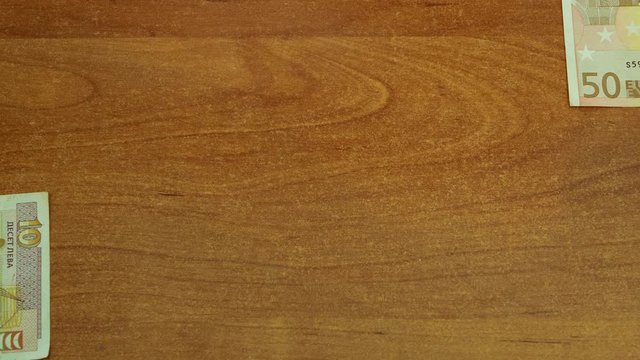 stop motion animation of 50 euros and 10 Bulgarian lev on wooden desk. banknotes moving from different sides, meet at middle for a second and then moving out of sight. looped closeup 4k video