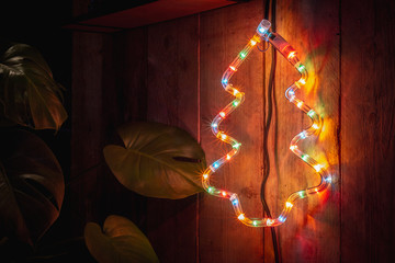 Christmas decoration with colored lights in the shape of a Christmas tree hanging on a wooden wall
