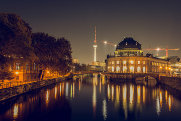 Obraz premium Berlin skyline at night. museum island with river spree and bridges are illuminated in autumn mood. in the background is the TV tower. A path with trees on the river bank. the lights reflect in the wa